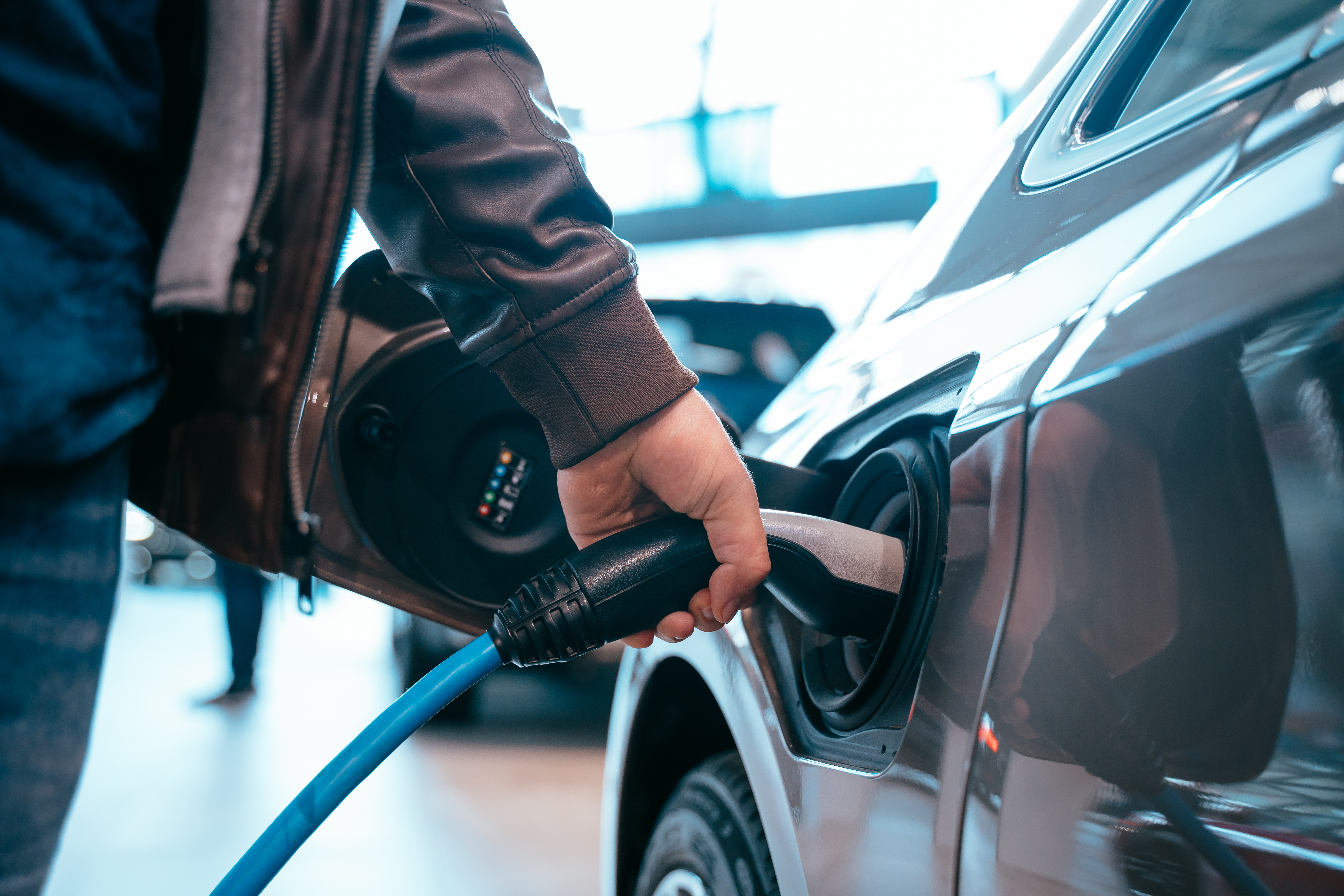 Human hand is holding Electric Car Charging connect to Electric car