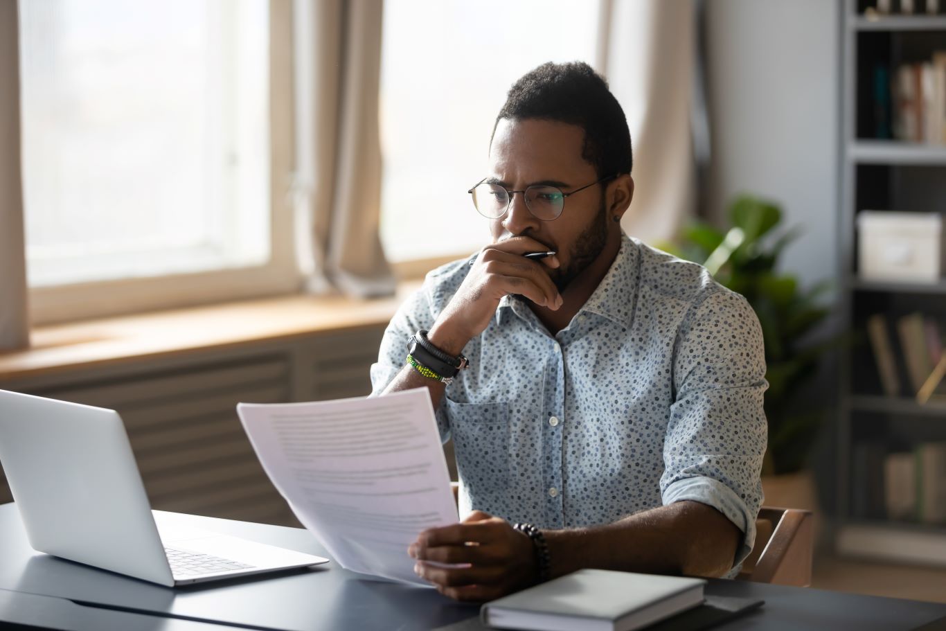 Thoughtful young mixed race businessman in glasses holding paper document Thoughtful young mixed race businessman in glasses holding paper document