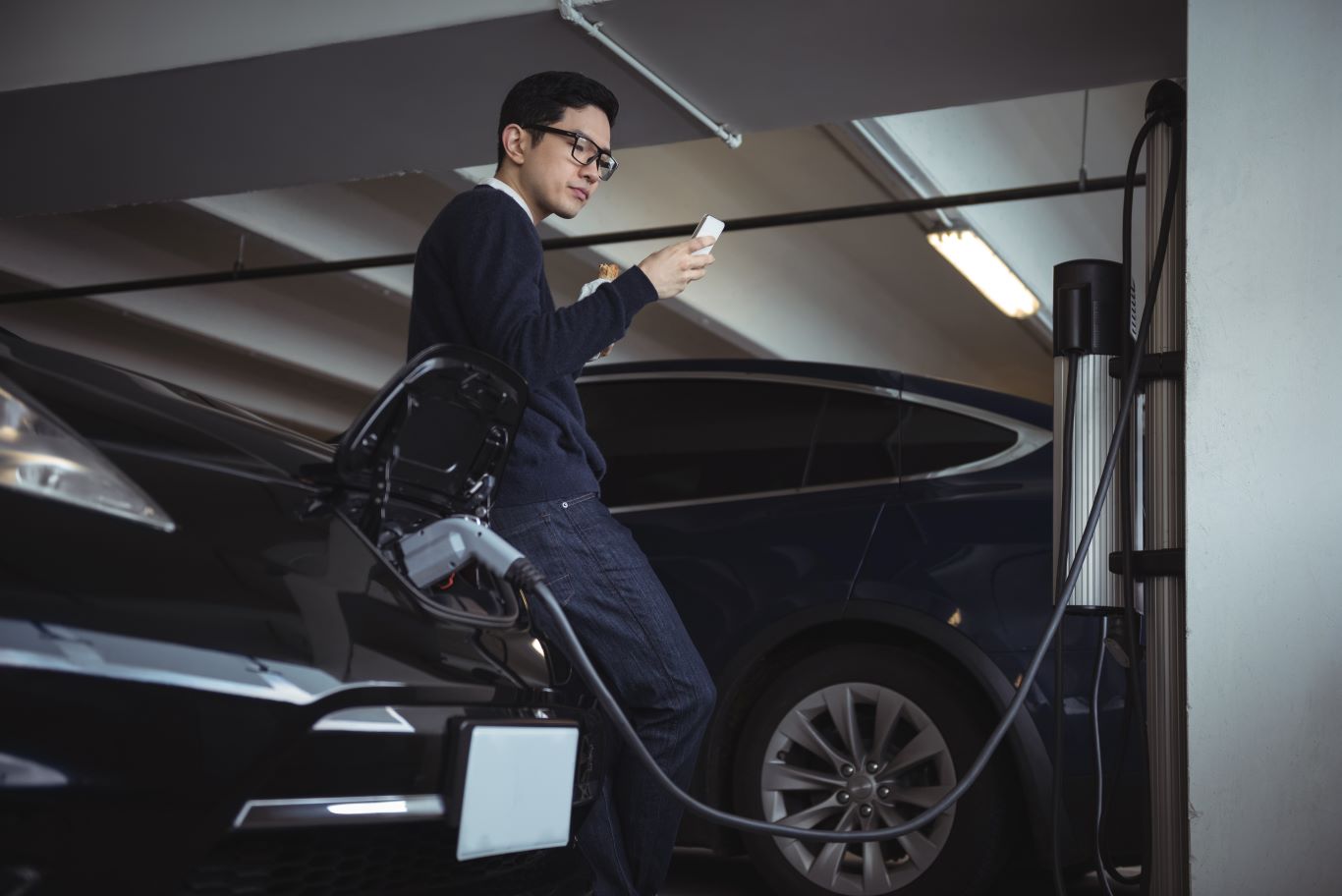 Man using mobile phone while charging electric car Man using mobile phone while charging electric car