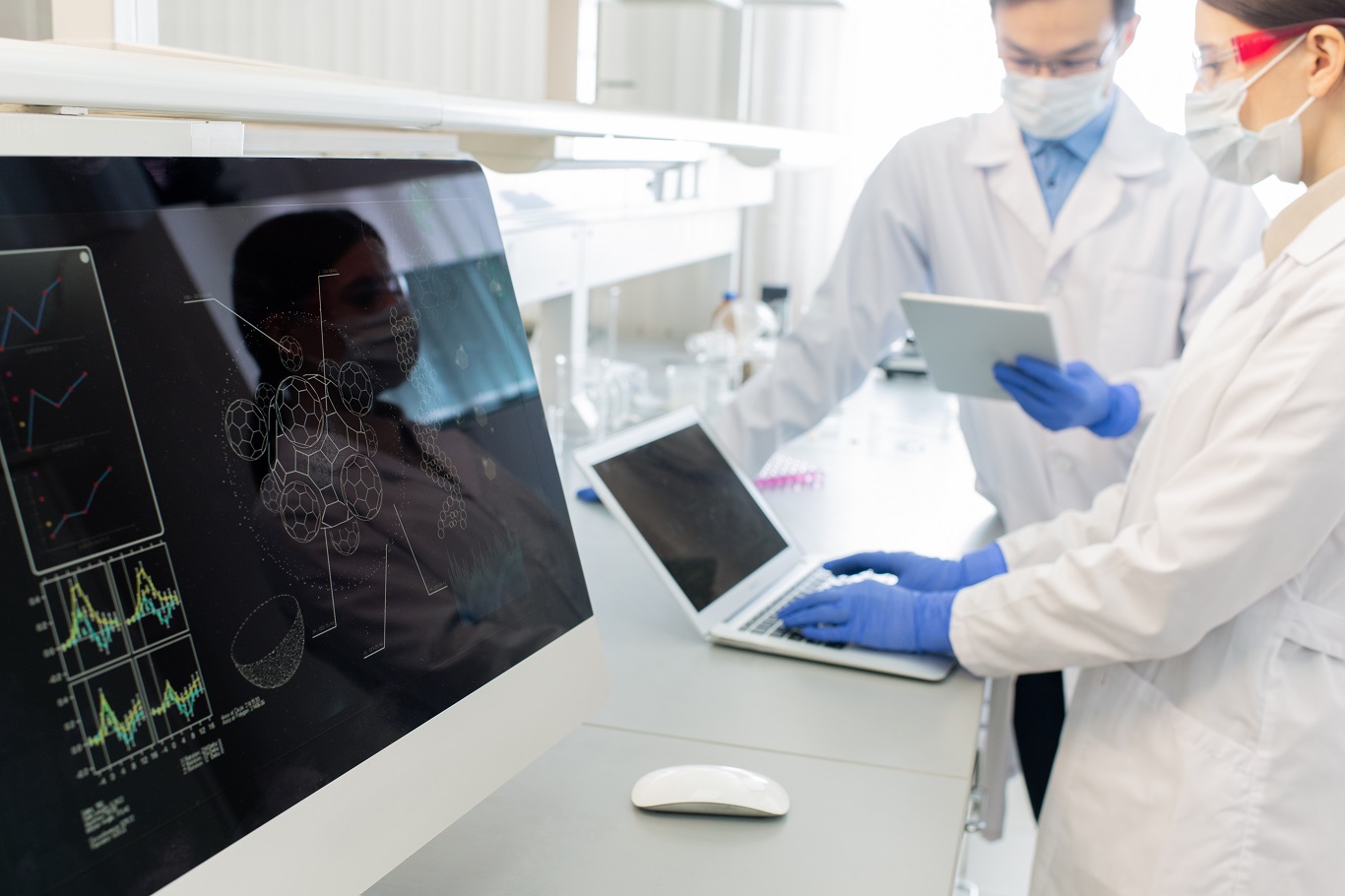 Computer screen with molecule model on background of two lab workers in whitecoats Computer screen with molecule model on background of two lab workers in whitecoats