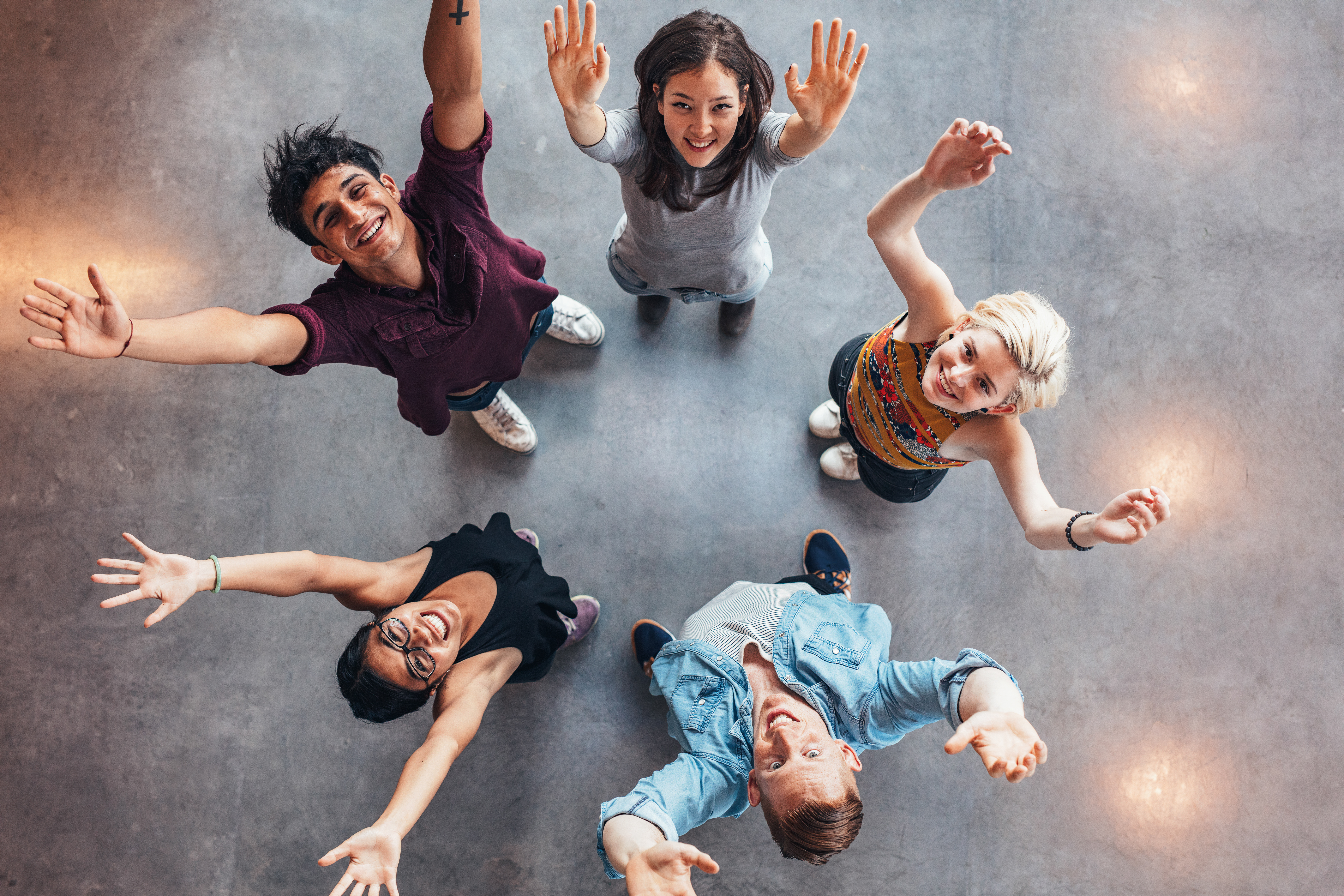 Top view of young students standing together looking up at camera with their hands raised in celebration Top view of young students standing together looking up at camera with their hands raised in celebration