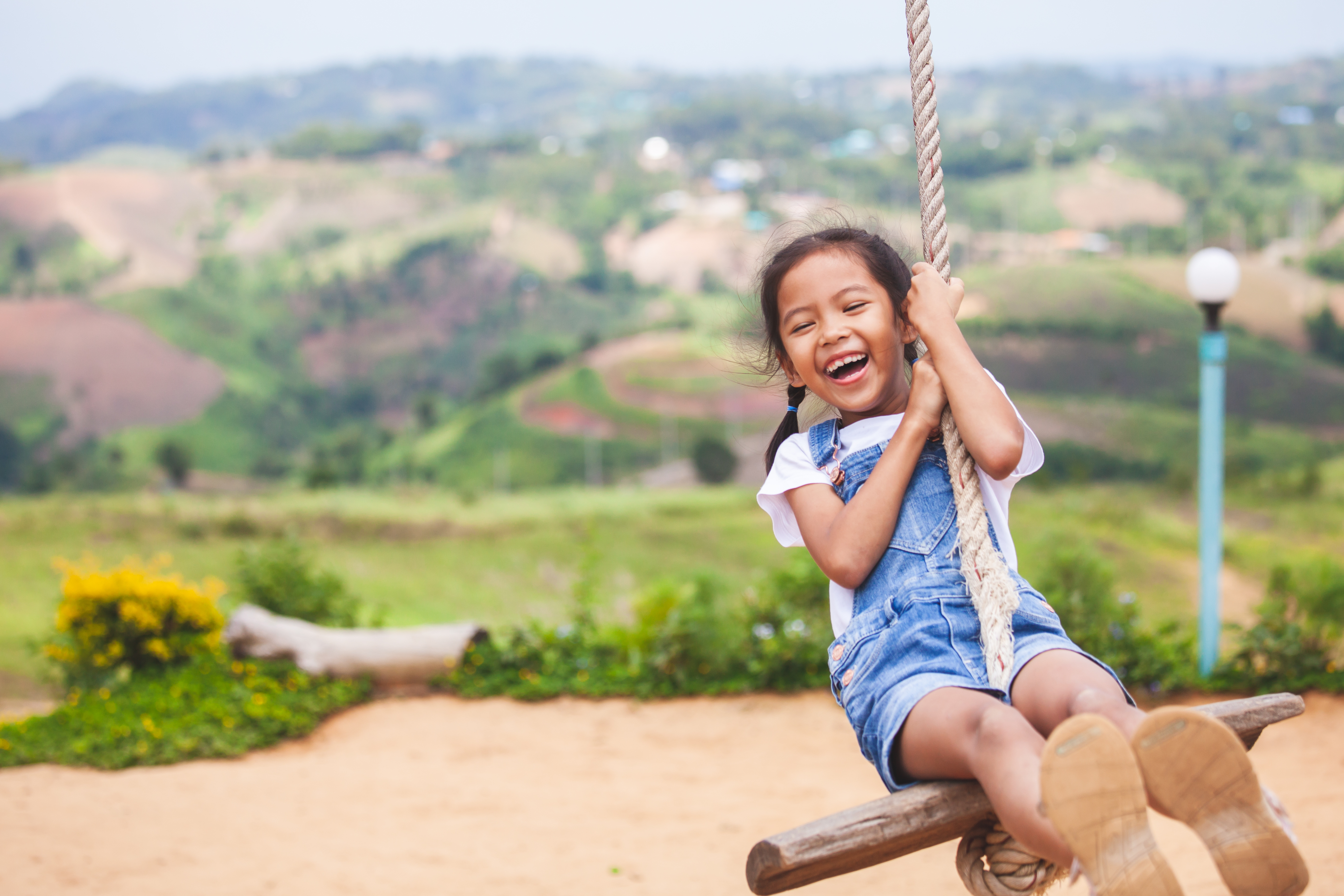 Happy asian child girl having fun to play on wooden swings in playground with beautiful nature Happy asian child girl having fun to play on wooden swings in playground with beautiful nature