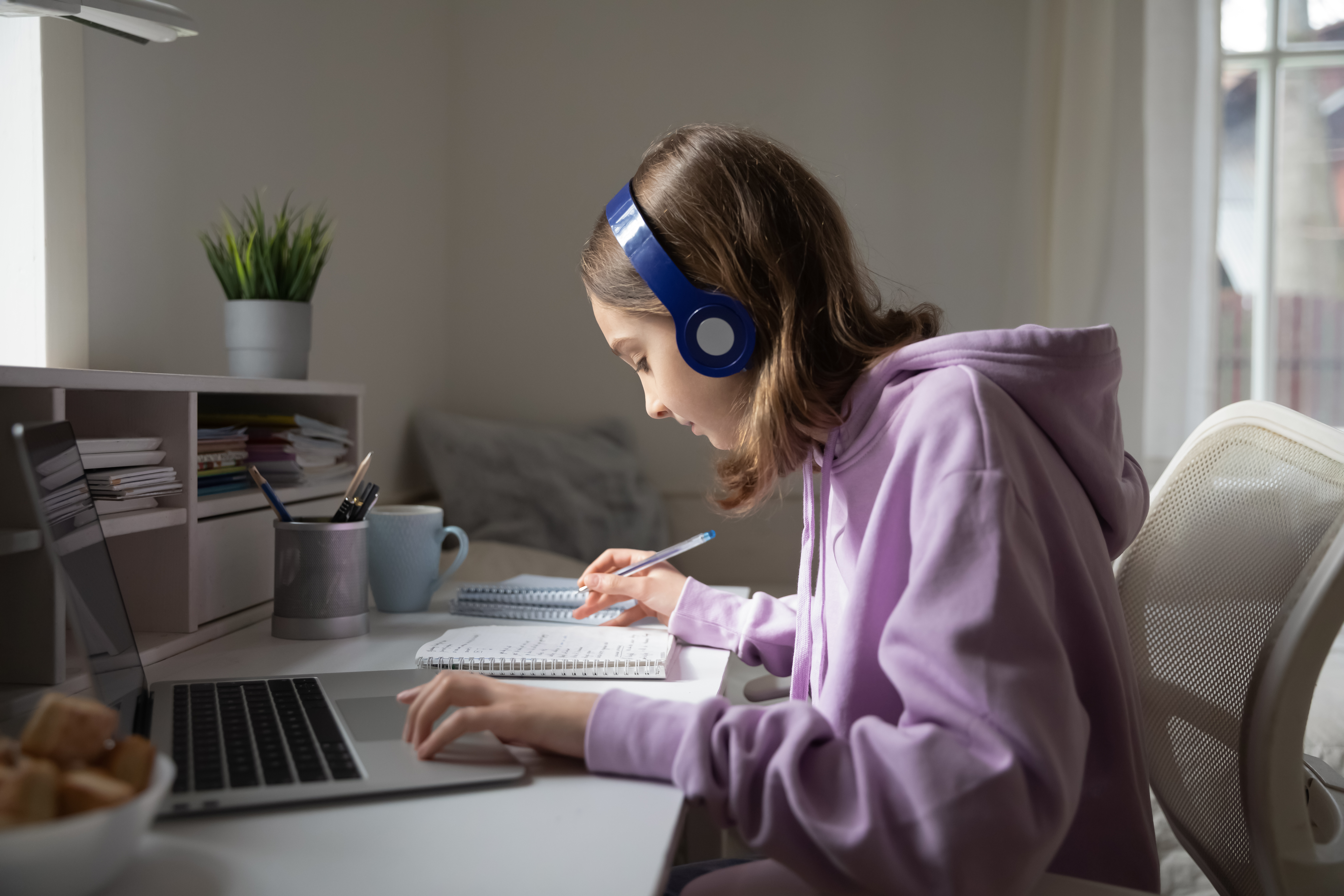 Teen girl school pupil wearing headphones studying online from home making notes