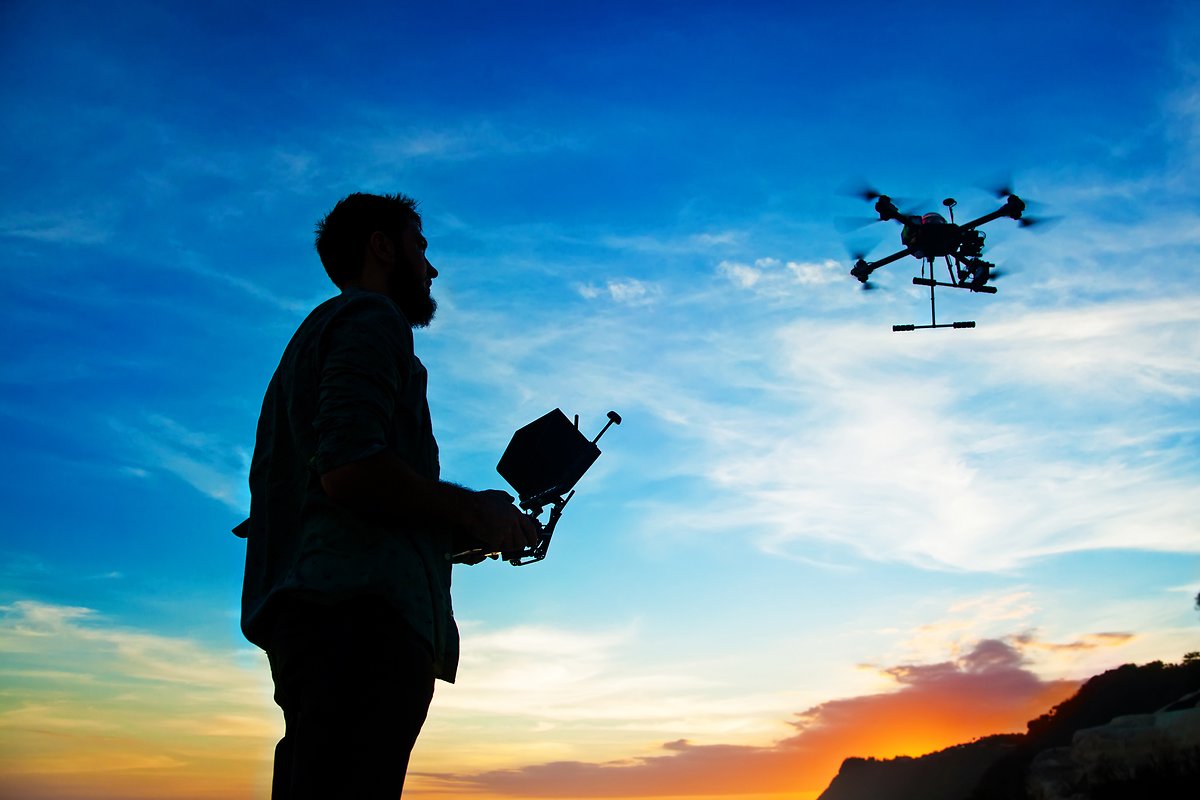 Man playing with a drone against sunset sky